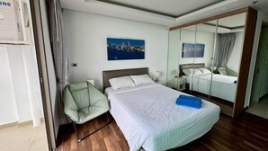 A hotel room with a large bed, a chair, a mirror, and a painting on the wall. - The Peak Towers by PSR (Pattaya)