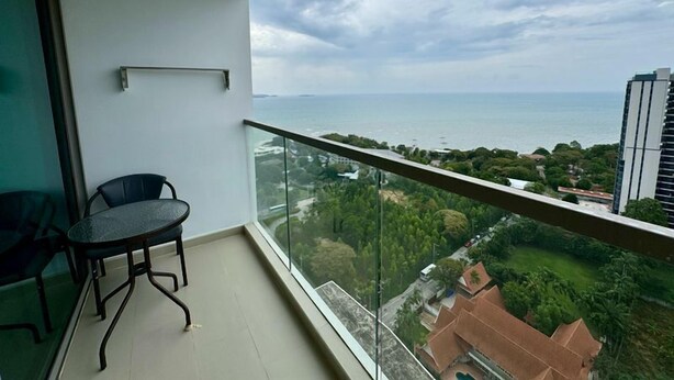 A balcony with a glass railing overlooking a coastal view, a table, and a chair. - The Peak Towers by PSR (Pattaya)