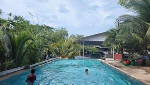A swimming pool with clear water, surrounded by lush greenery and a covered area in the background. - Monkey House Hostel Koh Samui (Koh Samui)
