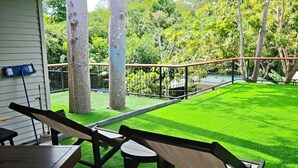 A covered patio with a wooden deck, a grassy lawn, and a metal fence. - Monkey House Hostel Koh Samui (Koh Samui)