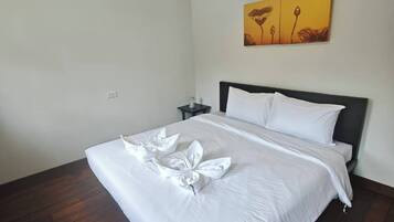 A hotel room with a bed, a nightstand, a painting on the wall, and wooden flooring.