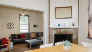 A living room with a sofa, ottoman, and a dining table with chairs. There is a fireplace with a stone mantle and a mirror above it.