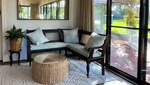 Ein gemütlicher Sitzbereich mit einer Couch und Sesseln, einem großen Spiegel und Blick auf einen Garten durch eine Glastür.