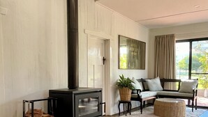 Ein modernes Wohnzimmer mit einem schwarzen Kaminofen, einer Couch, einem Sessel und einem großen Fenster.