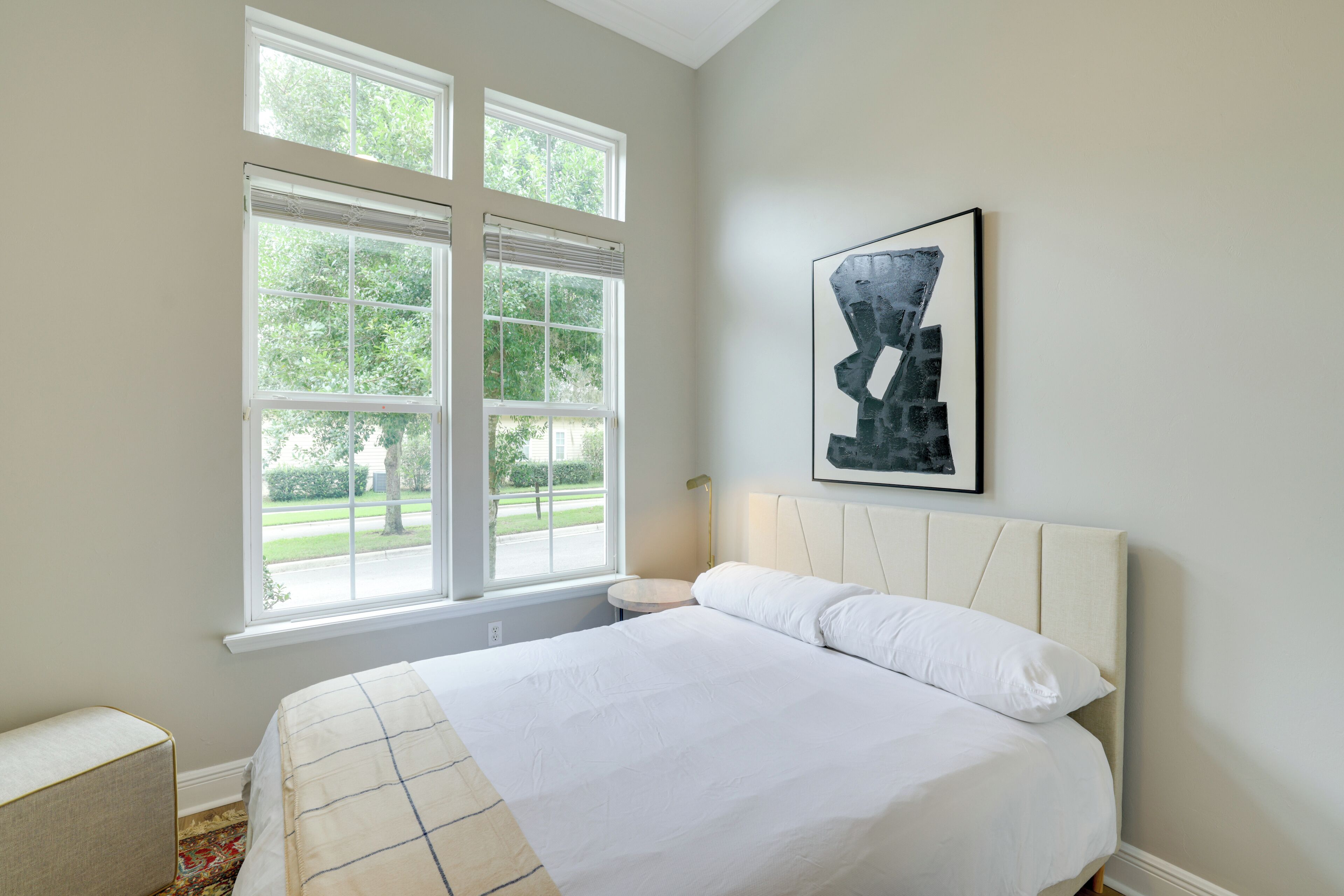 A bedroom with a large bed, a nightstand, a lamp, and a window with a view of greenery.