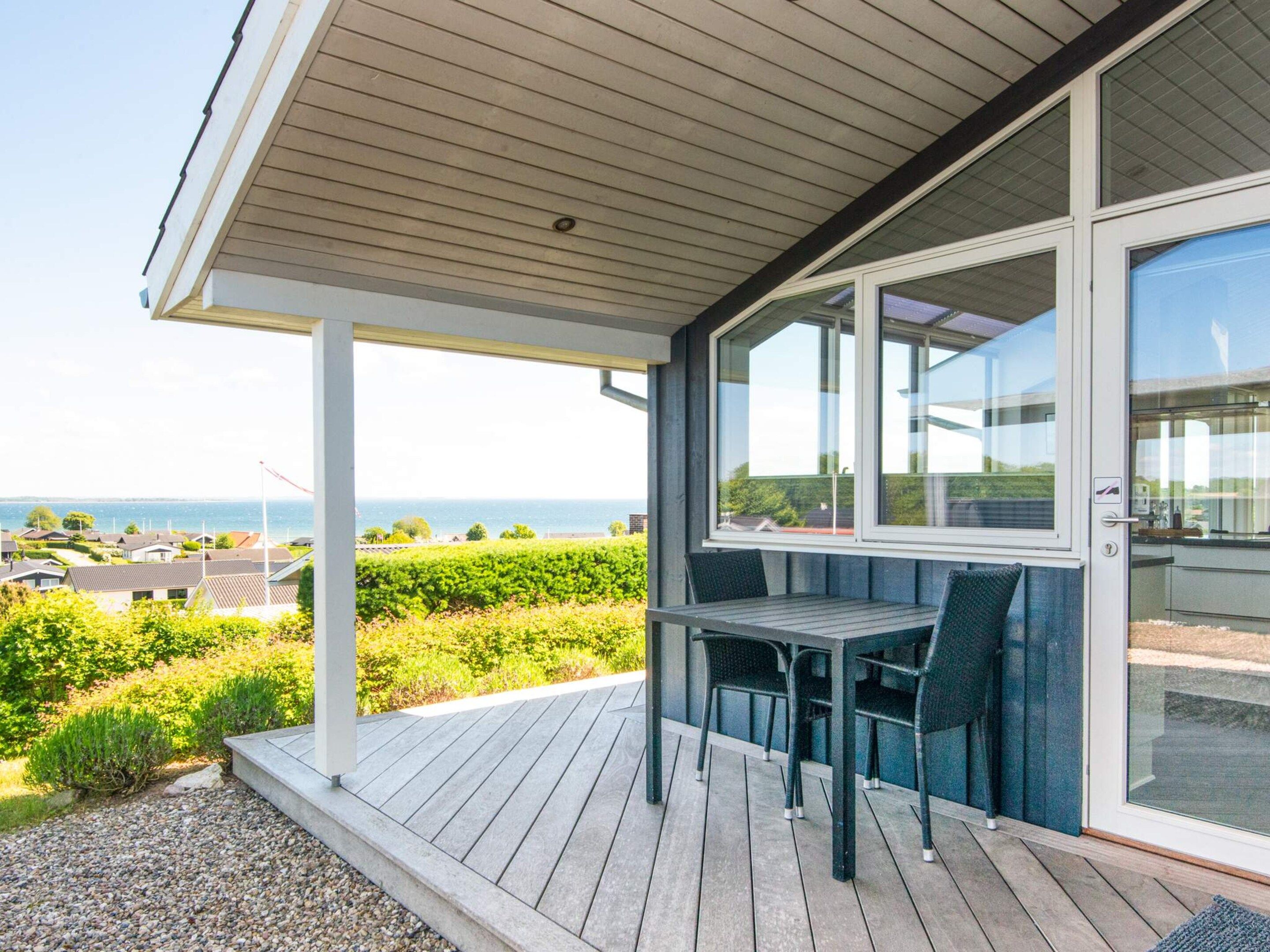 A covered outdoor area with a table and chairs, a view of the sea, and a vineyard in the background.