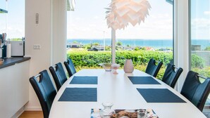 Un comedor moderno con una gran mesa, sillas negras y vista al mar.