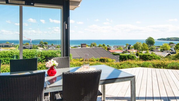 Un espacio de estar al aire libre techado con mesa y sillas, con vistas a una zona residencial y al mar.