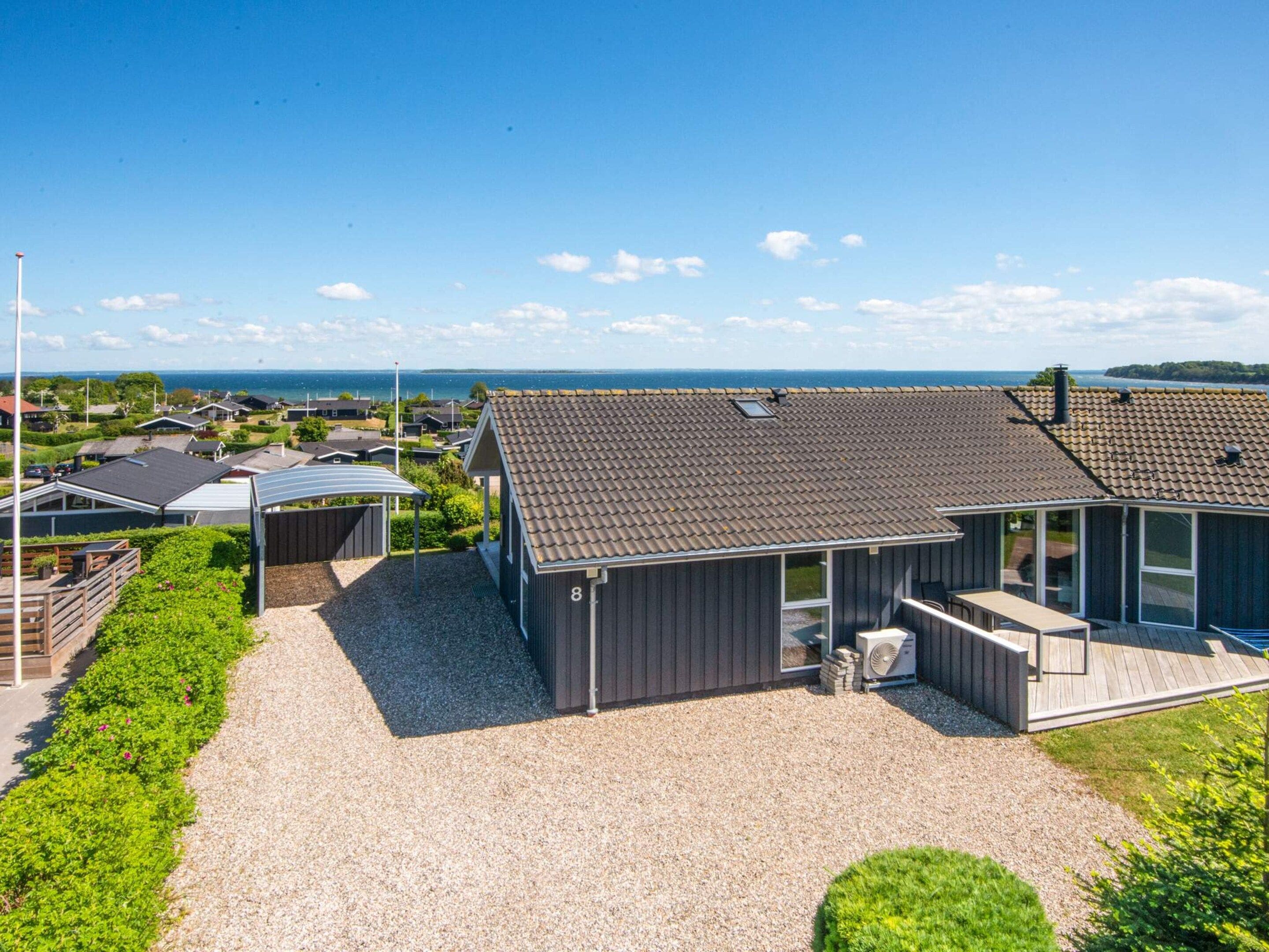 A modern house with a gravel driveway, a covered patio, and a view of the sea.
