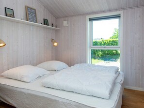 A bedroom with a bed, a window, and a shelf with pictures.