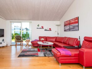 A modern living room with a red leather sofa, a round coffee table, and a large window offering a view of greenery outside.