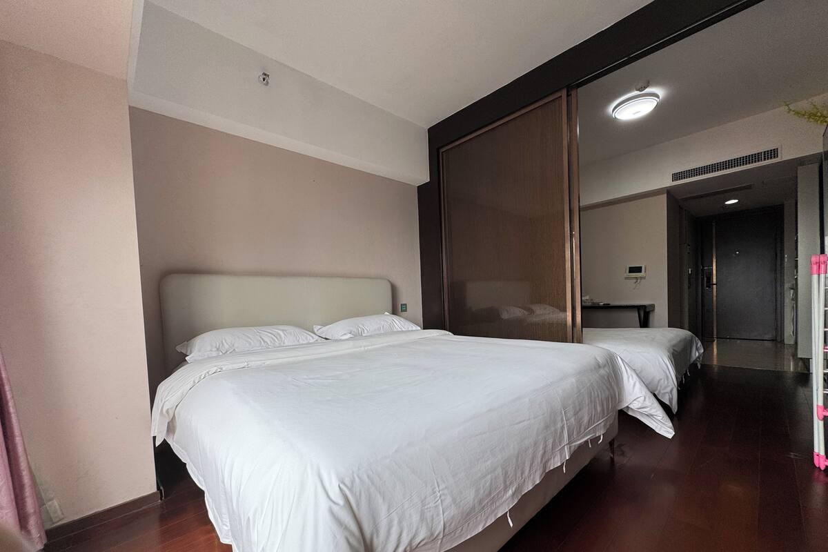 Une chambre d’hôtel avec deux lits, un grand miroir, un plancher en bois et une porte donnant sur une autre pièce.