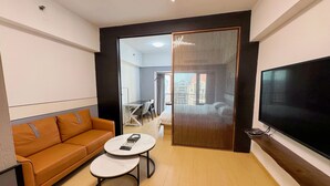 A modern hotel room with a sofa, two round tables, a TV, and a view of the city through a large window. - Linjiang Shangpin Apartment (Guangzhou)