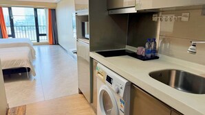A hotel room with a bed, a washing machine, a sink, and a view of the city. - Linjiang Shangpin Apartment (Guangzhou)