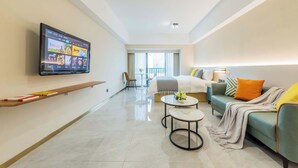 A modern living room with a flat-screen TV mounted on the wall, a sofa with cushions, a coffee table, and a balcony with a view. - Linjiang Shangpin Apartment (Guangzhou)