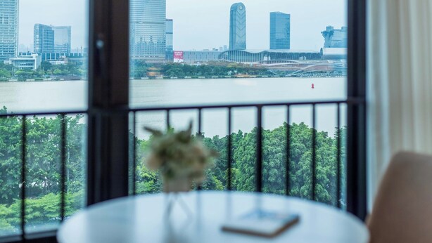 A view from a room with a large window overlooking a cityscape and a body of water. - Linjiang Shangpin Apartment (Guangzhou)