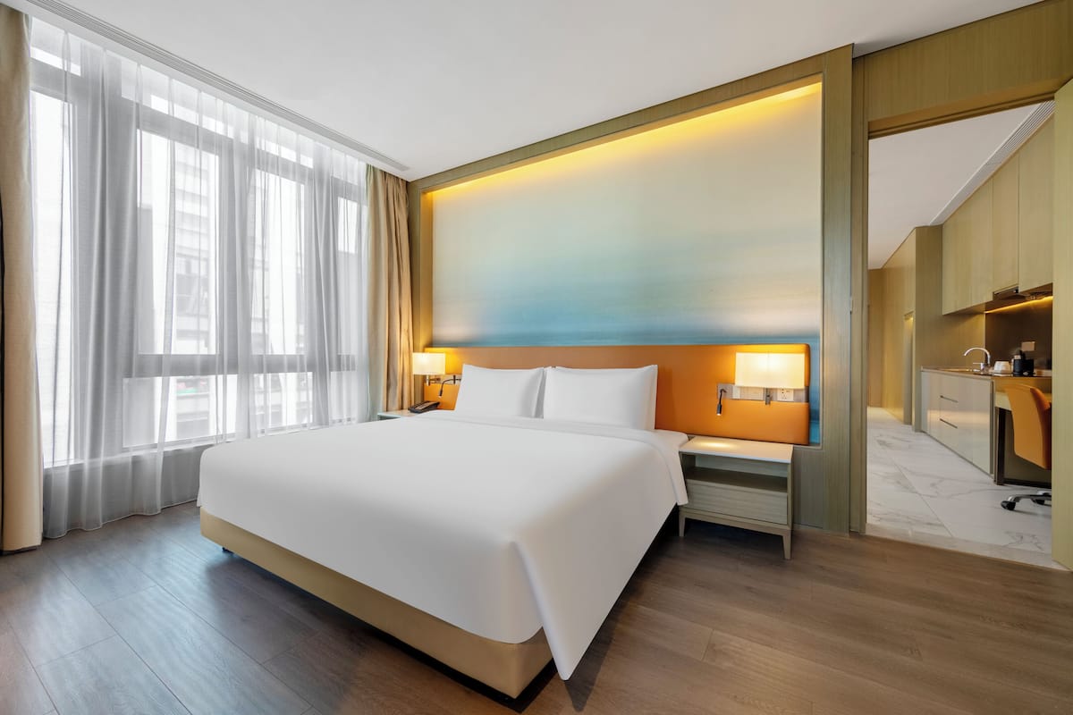 Habitación de hotel con una cama grande, mesitas de noche, un escritorio, una silla, un espejo y vistas al exterior por la ventana.