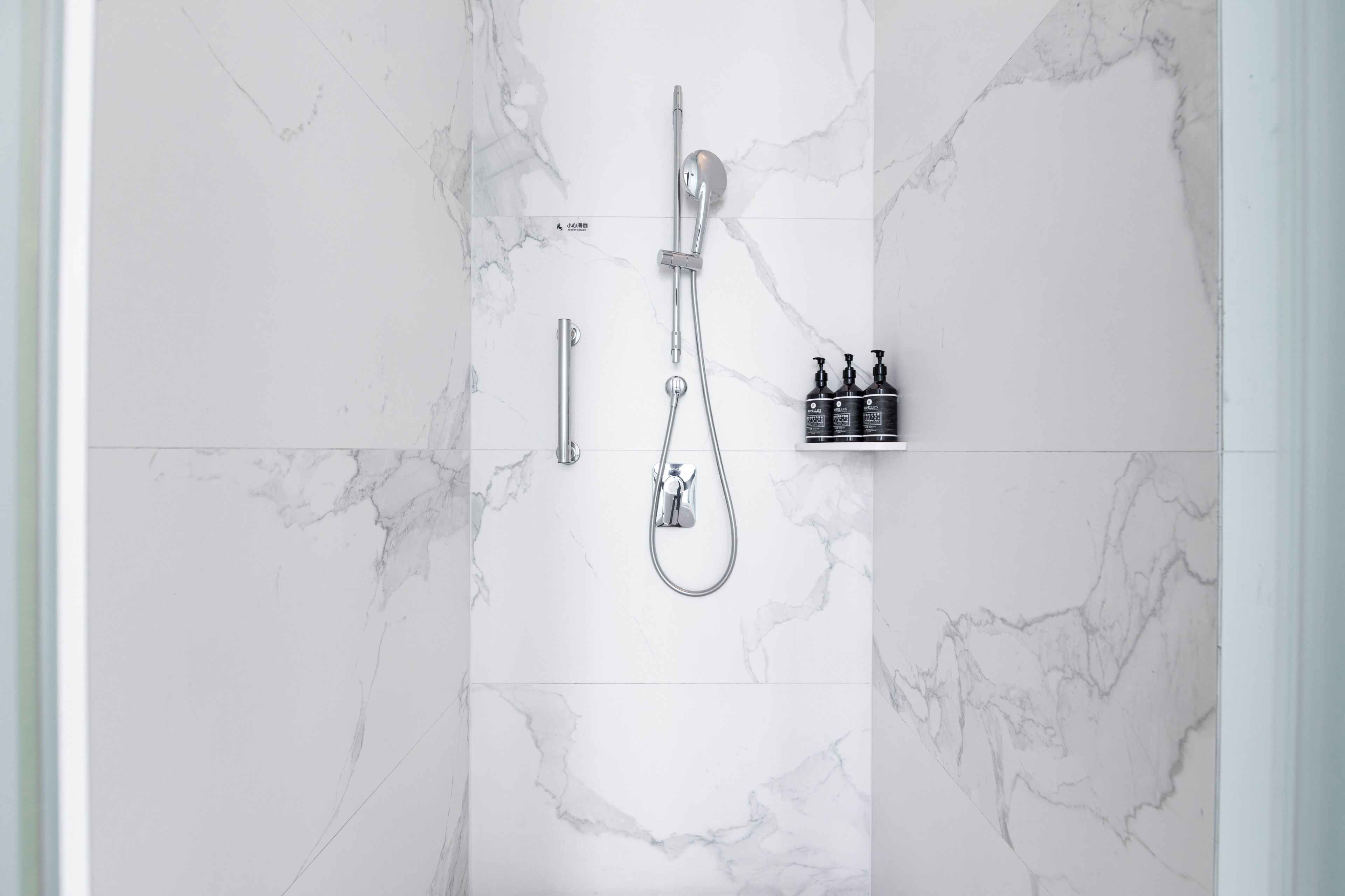 Een badkamer met een douche, douchetuit, wandkraan en een plank met toiletartikelen.