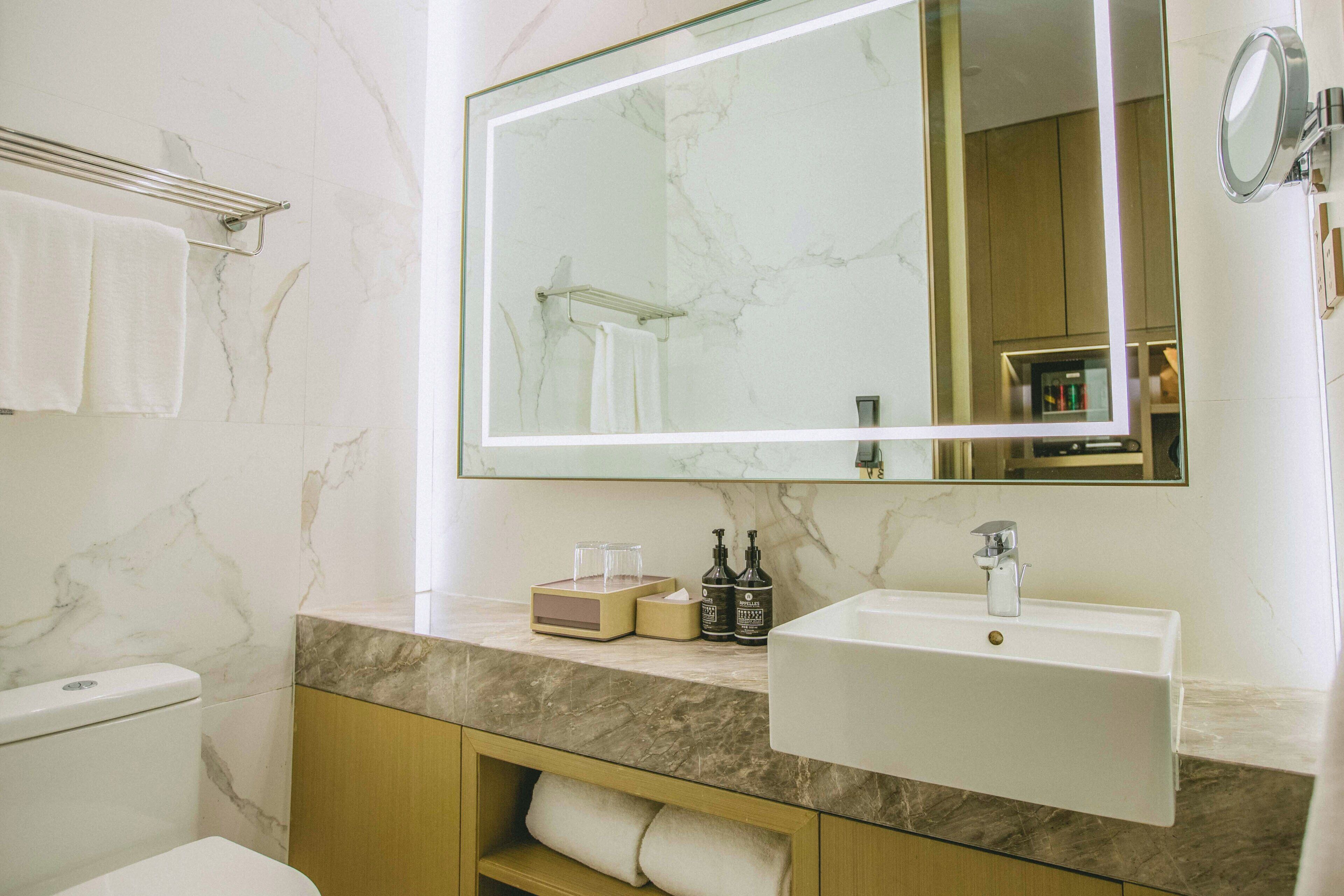A bathroom with a marble wall, a large mirror, a sink, and a towel rack.