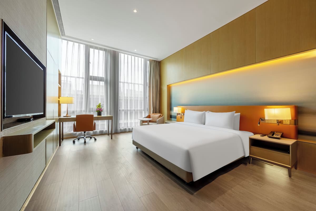 Una habitación de hotel moderna con una cama grande, un escritorio, una silla, un televisor y una mesita de noche con una lámpara.