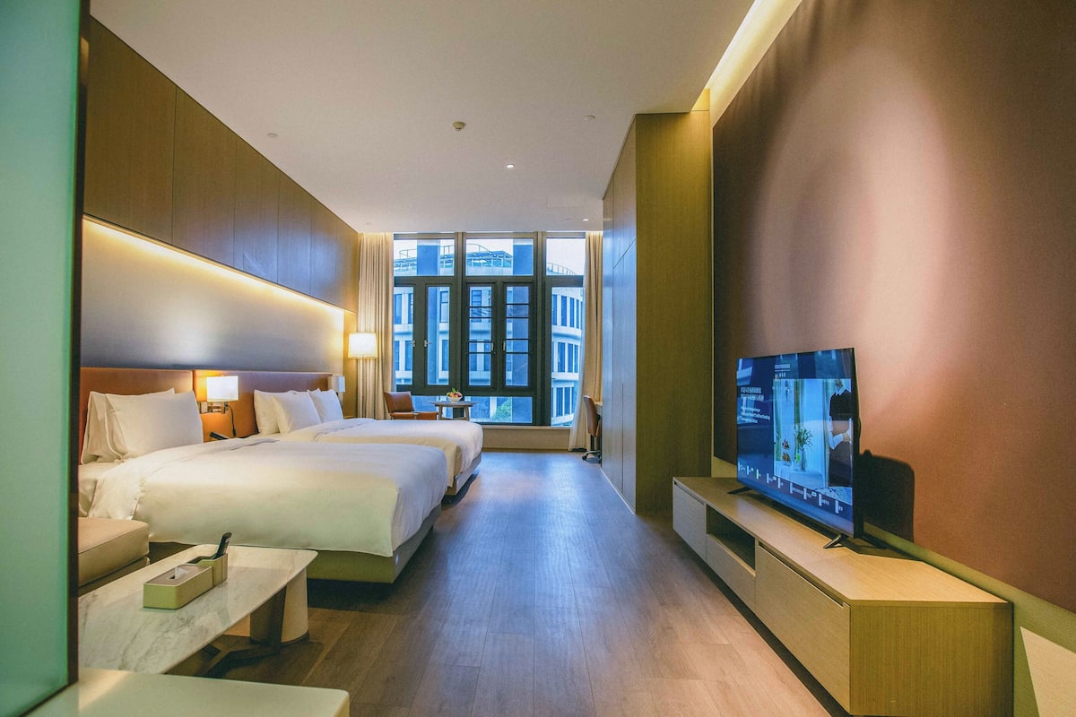 Habitación de hotel con una cama grande, televisión, escritorio y ventana con vista a la ciudad.
