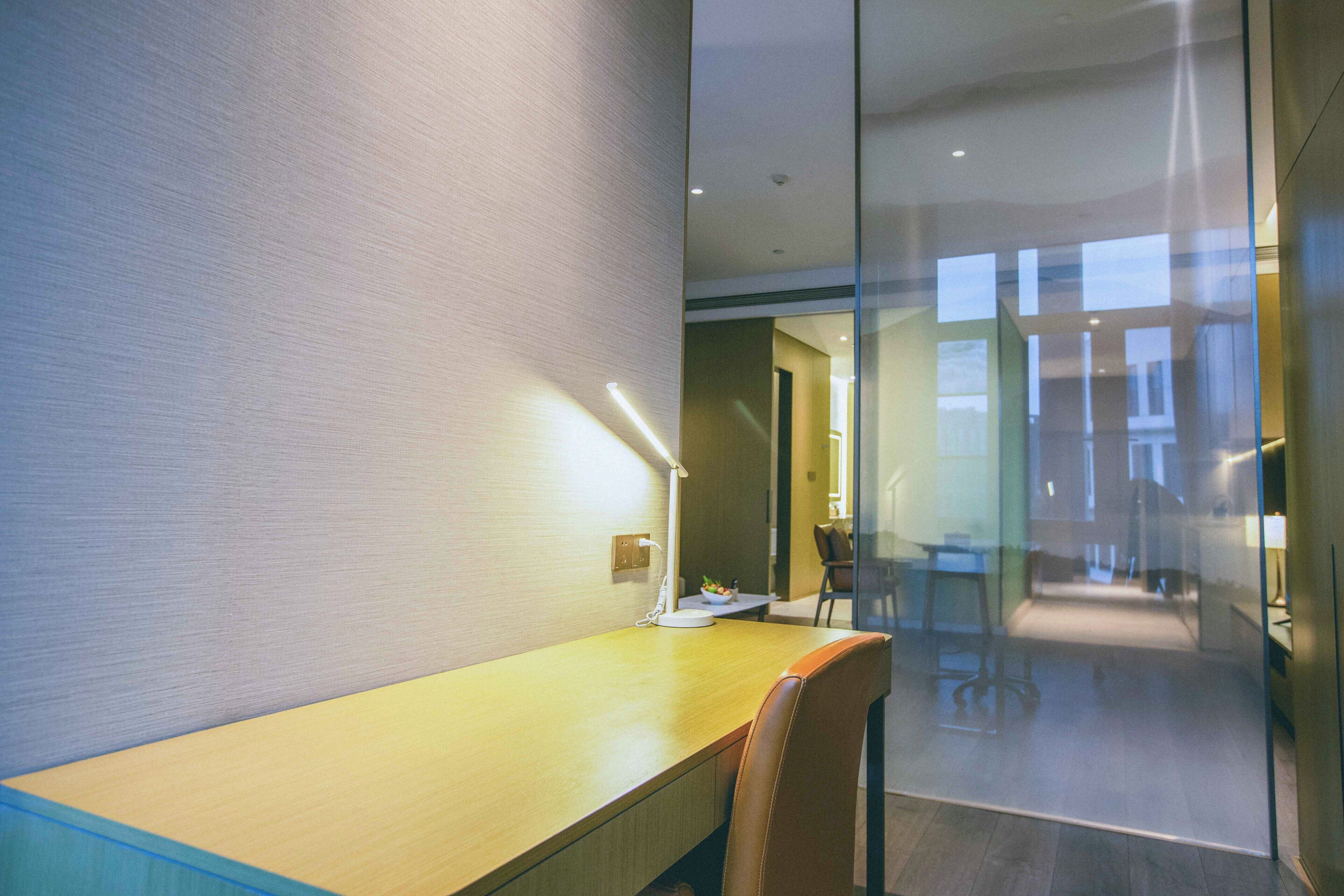 A modern office space with a wooden desk, a chair, and a glass partition.