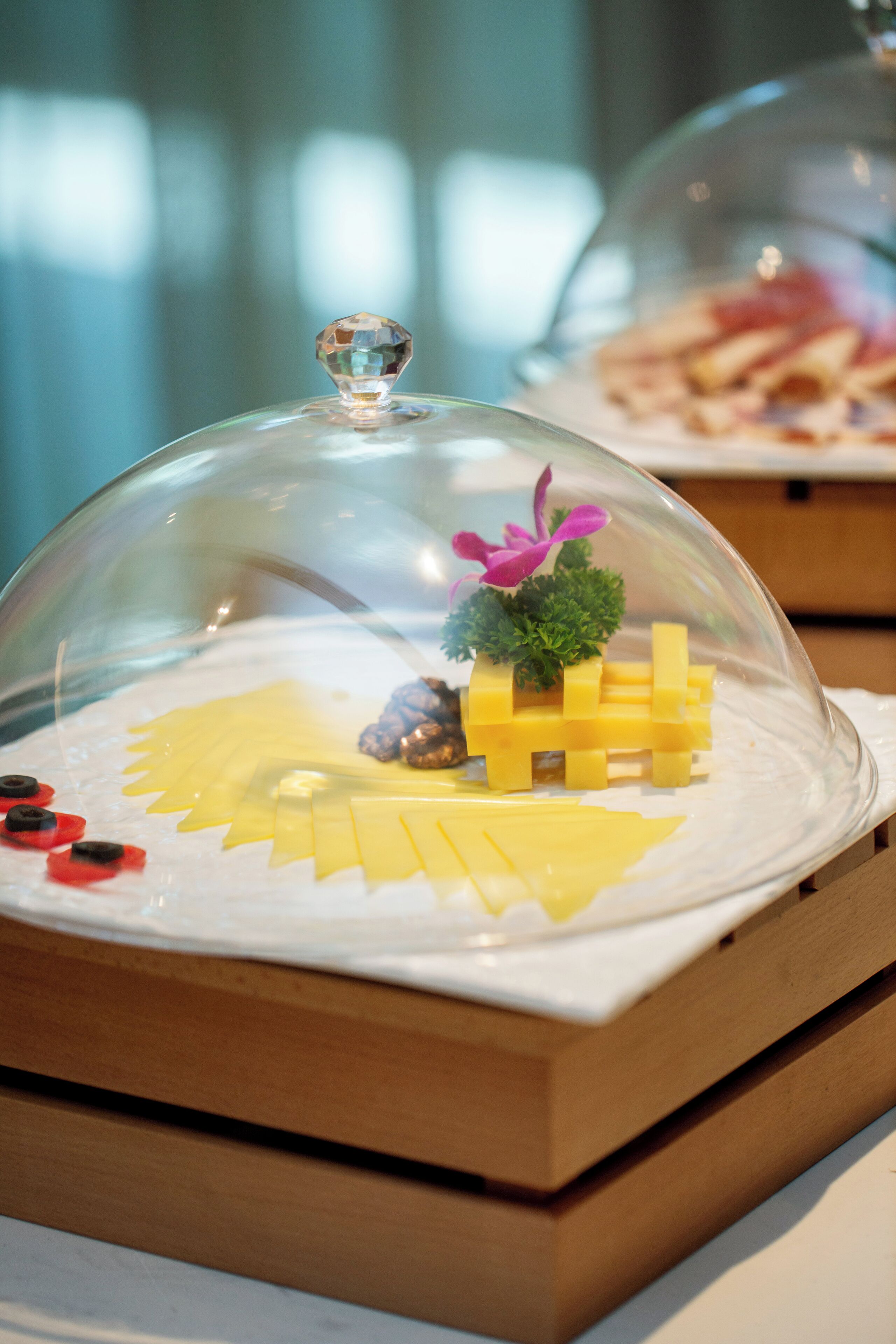 A dessert display with a glass dome, featuring a yellow cheese arrangement and decorative elements.