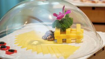 A dessert display with a glass dome, featuring a yellow cheese arrangement and decorative elements.