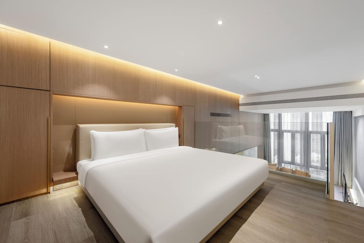 Una habitación de hotel moderna con una cama grande, paneles de madera y un amplio ventanal con cortinas.