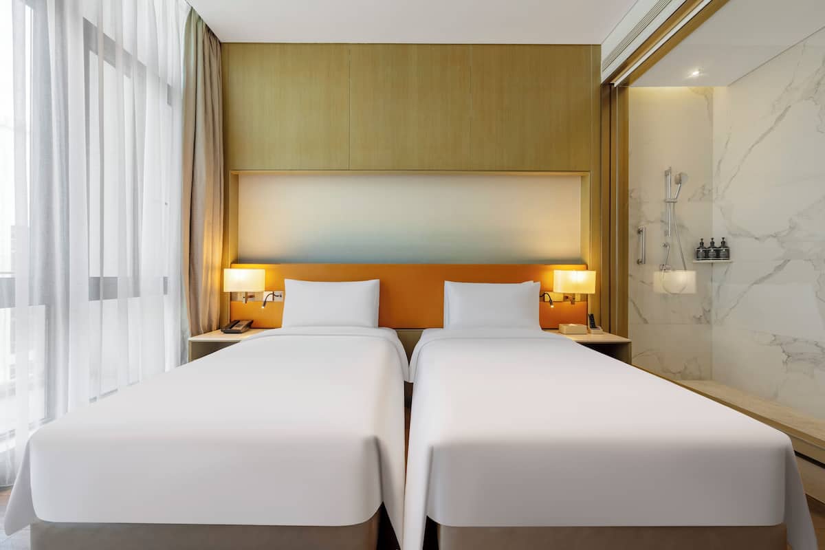 Habitación de hotel con dos camas, cabecera de madera, paredes de mármol y zona de ducha.