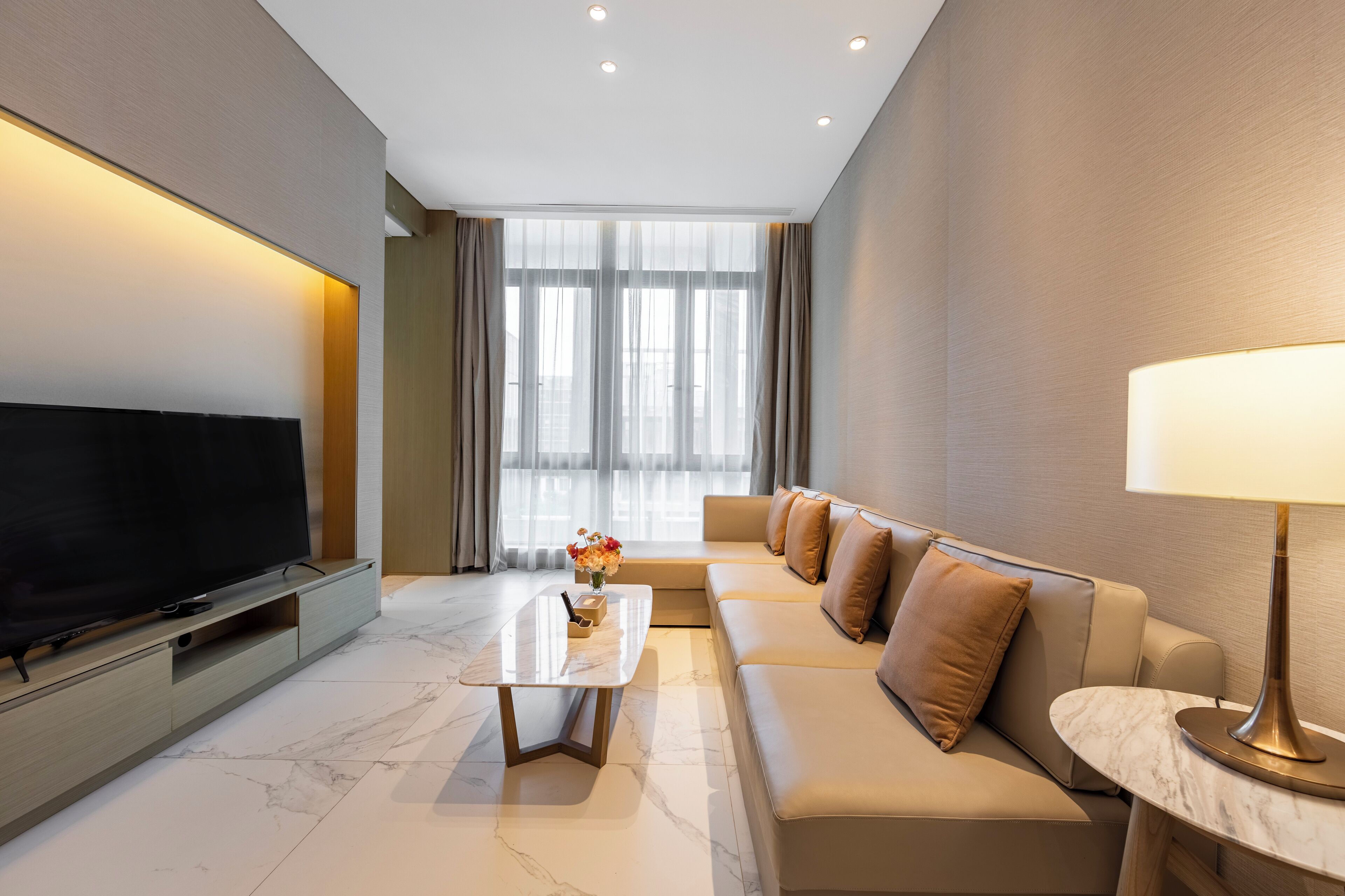 A modern living room with a flat-screen TV, a marble coffee table, a sofa set, and a lamp.