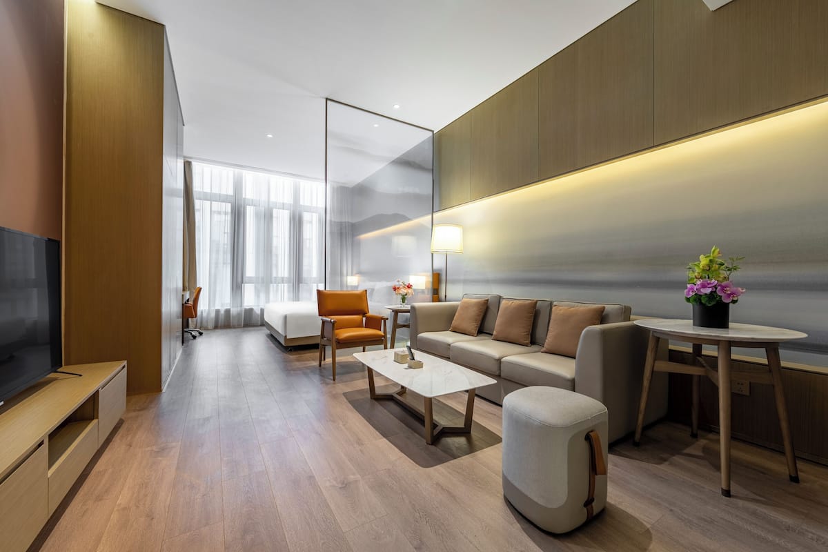 Una habitación de hotel moderna con sofá, sillón, mesa de centro y televisor.