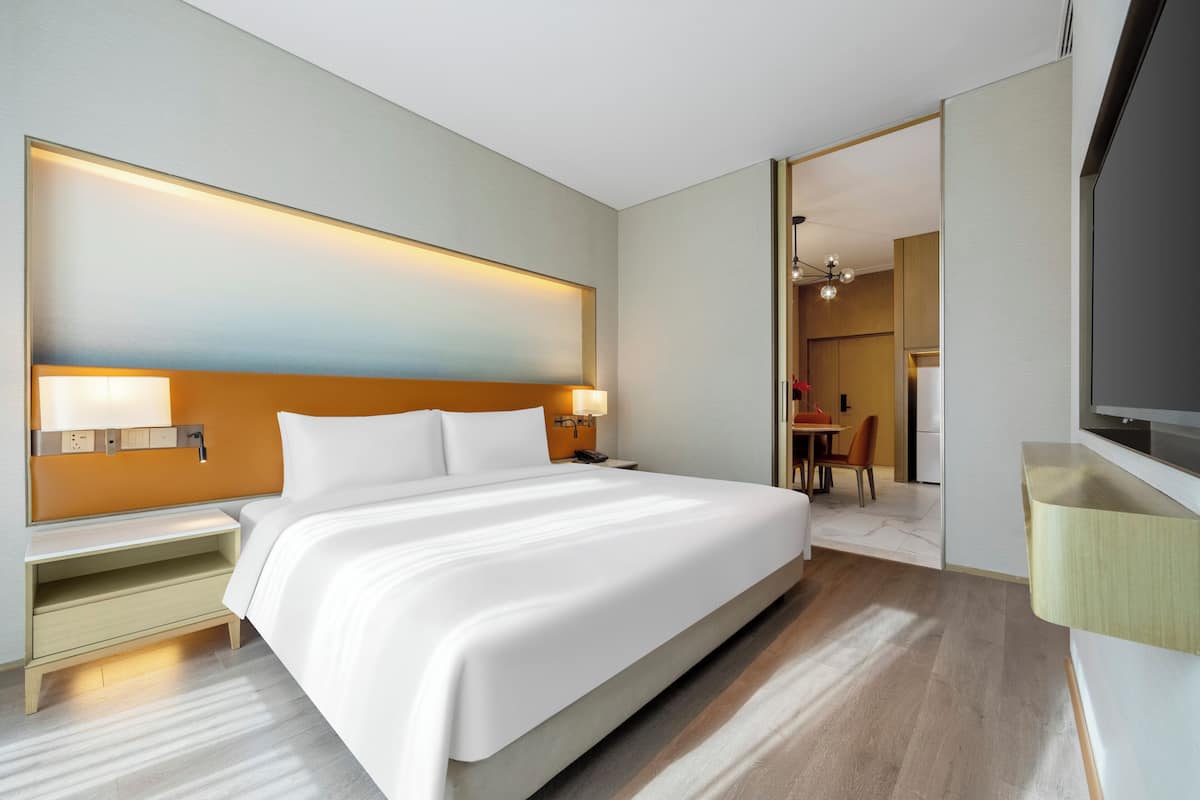 Habitación de hotel moderna con una cama grande, mesitas de noche, un televisor de pantalla plana y vistas al comedor.