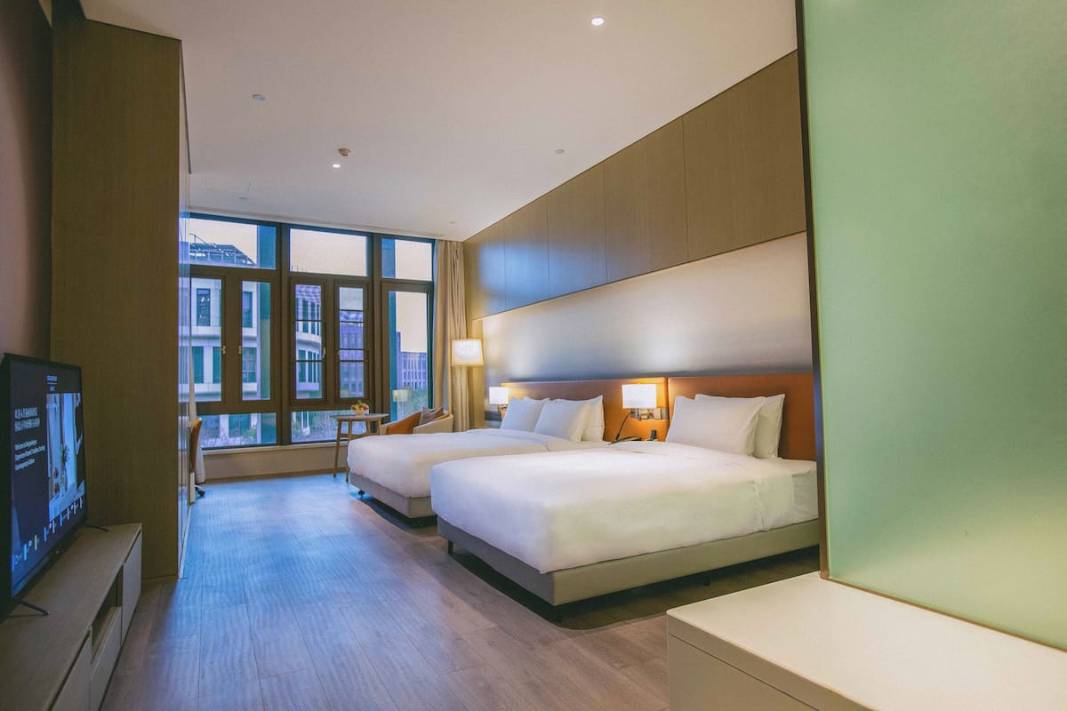 Habitación de hotel con dos camas, un televisor y un ventanal grande.