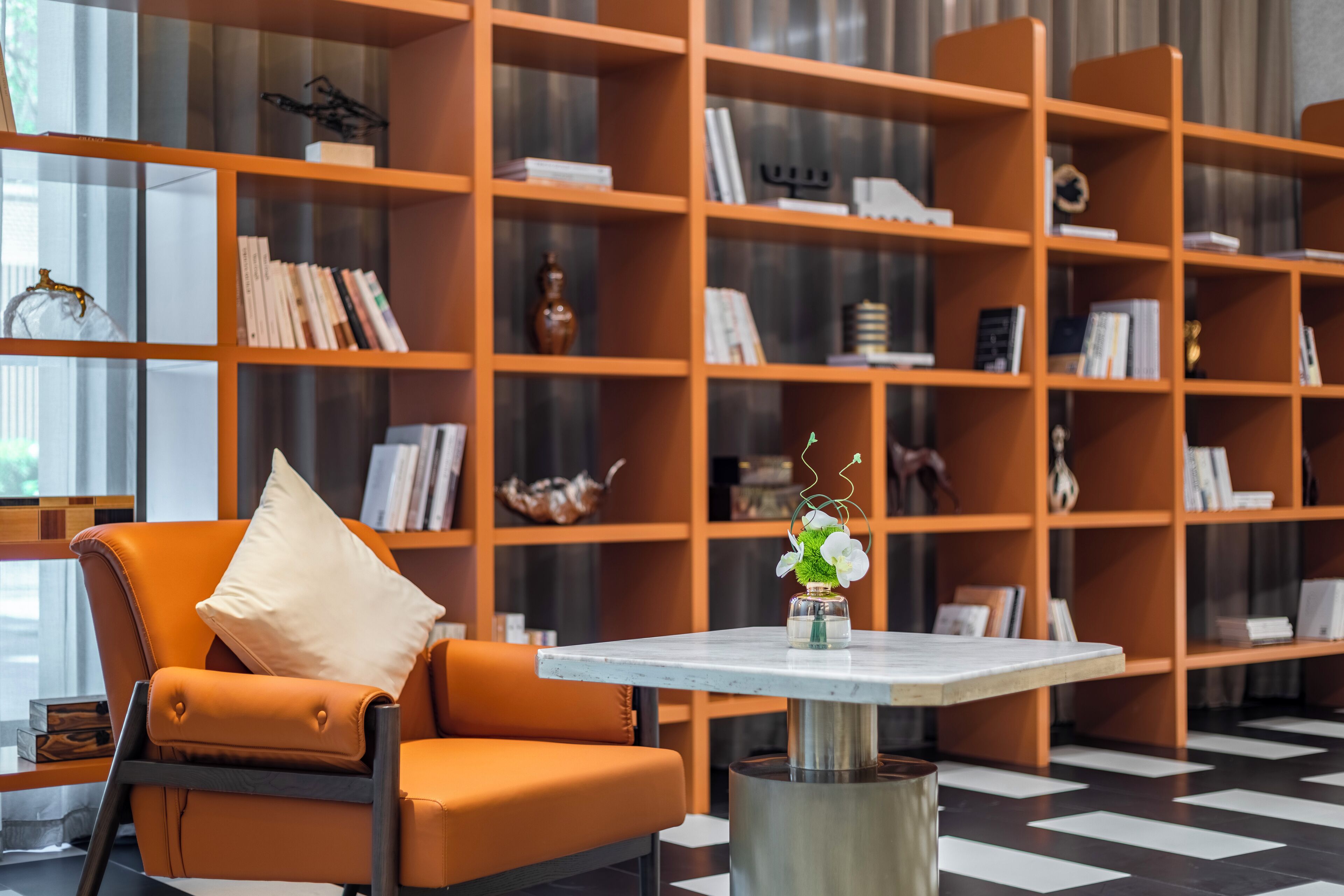 A modern library with a leather armchair, a marble table, and a large bookshelf filled with books and decorative items.