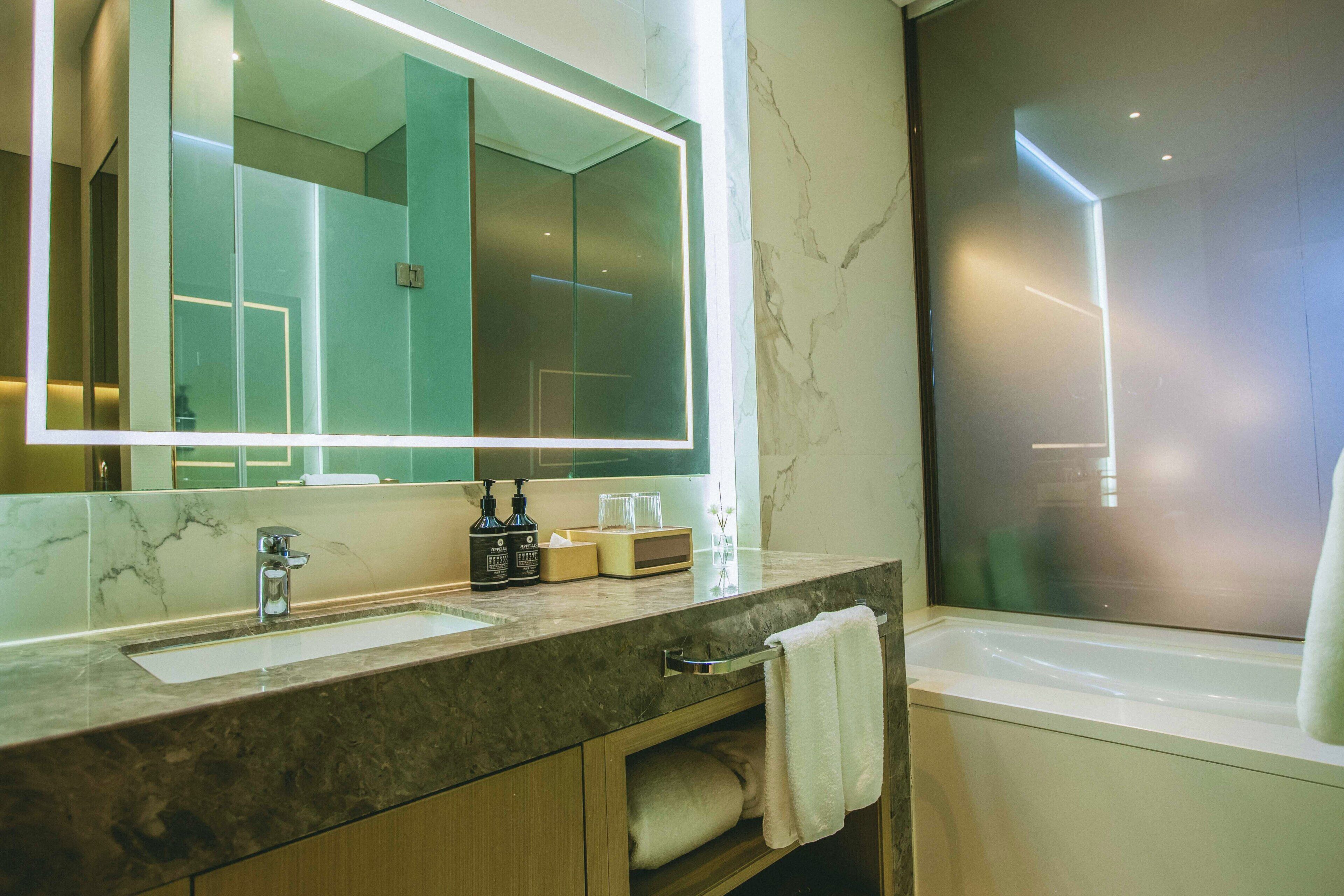 Une salle de bain moderne avec un grand miroir, un lavabo, une baignoire et un meuble-lavabo doté d’un porte-serviettes.