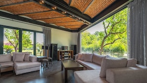 A spacious living room with a high ceiling, large windows, and a view of greenery outside. - Cottage House - Adult Only (Kemer)