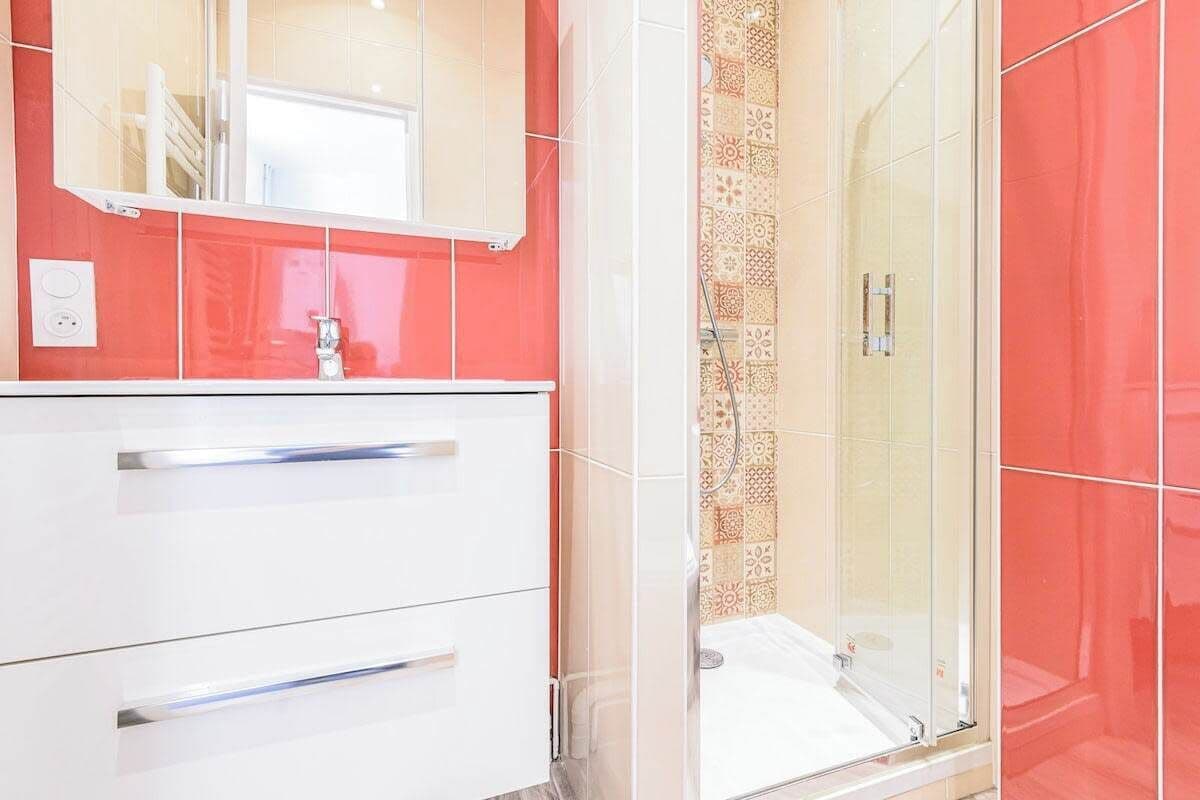 Une salle de bain avec un meuble-lavabo blanc, un miroir et un espace douche aux carreaux décorés.