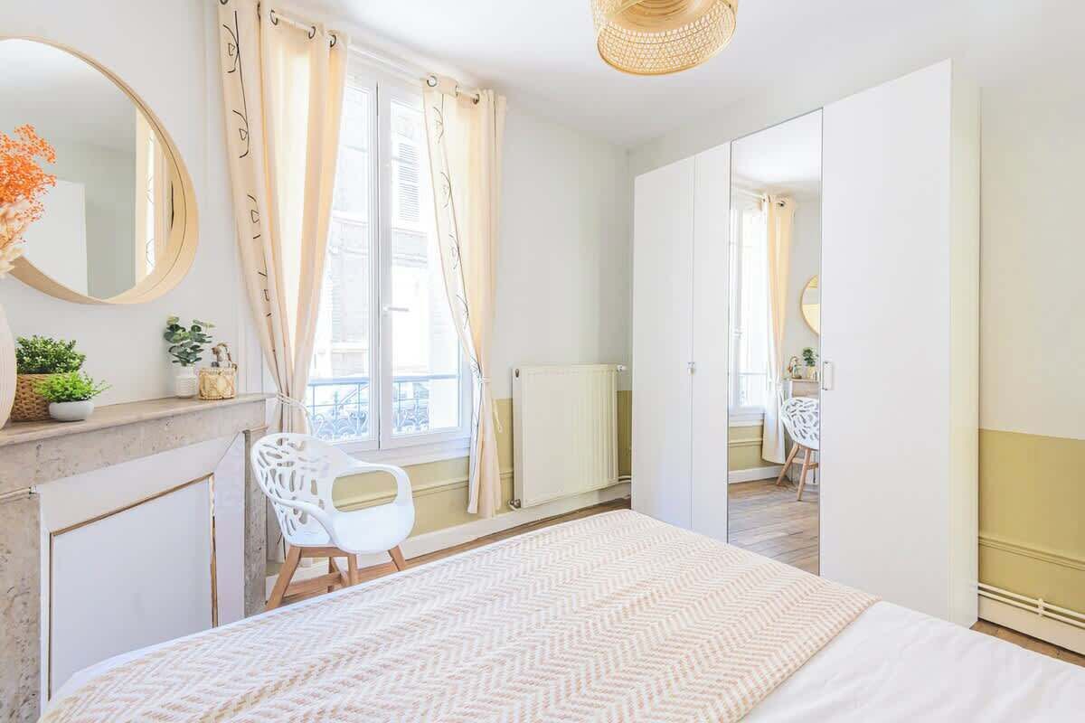 A bedroom with a bed, a dresser, a mirror, a window with curtains, and a radiator.