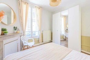 A bedroom with a bed, a dresser, a mirror, a window with curtains, and a radiator.
