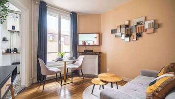 A modern living room with a sofa, a dining table with chairs, a fireplace, and a wall-mounted TV.