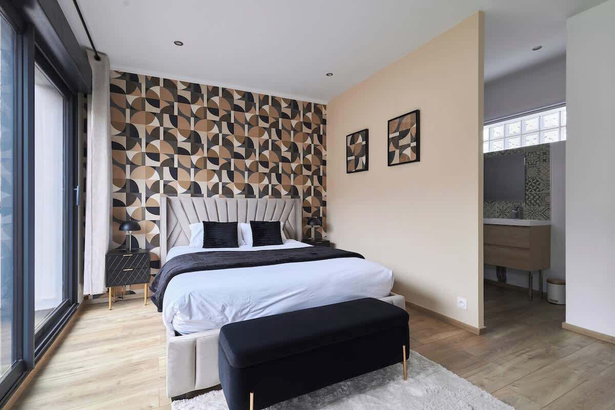 Une chambre à coucher moderne avec un grand lit, un banc et un mur orné d’un motif géométrique.