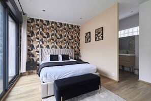 Ein modernes Schlafzimmer mit einem großen Bett, einer Bank und einer Wand mit geometrischem Muster.