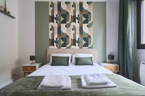 A neatly made bed with two pillows, a bedside table with a lamp, and a wall with a geometric pattern. - MM Suites Town House Terrasse (Reims)
