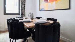 A dining area with a round table set for four, black chairs, a window with curtains, and a colorful abstract painting on the wall. - MM Suites Town House Terrasse (Reims)