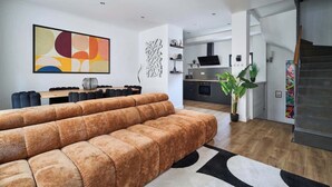 A modern living room with a large sectional sofa, a dining area with a table and chairs, a kitchen with a stove and cabinets, and a staircase leading to another level. - MM Suites Town House Terrasse (Reims)
