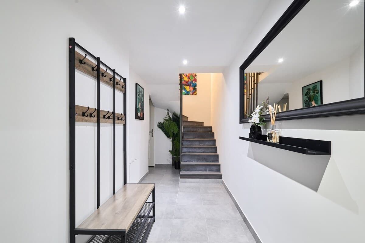 A modern hallway with a bench, a coat rack, a staircase, and a mirror.