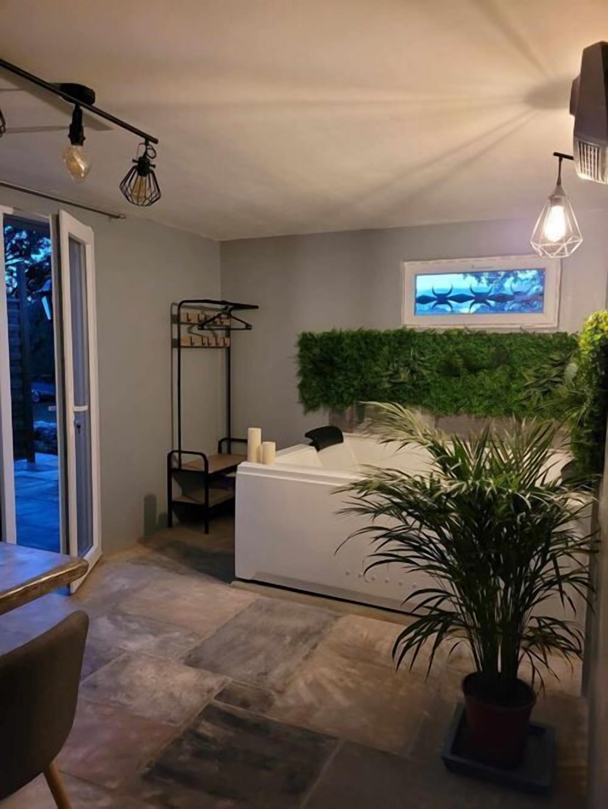 A modern bathroom with a bathtub, a green wall, and a potted plant.