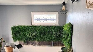 A modern bathroom with a large bathtub, a green wall-mounted plant, and a framed picture above the tub.