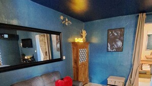 A living room with a blue wall, a grey sofa with red cushions, a wooden cabinet, and a small table.